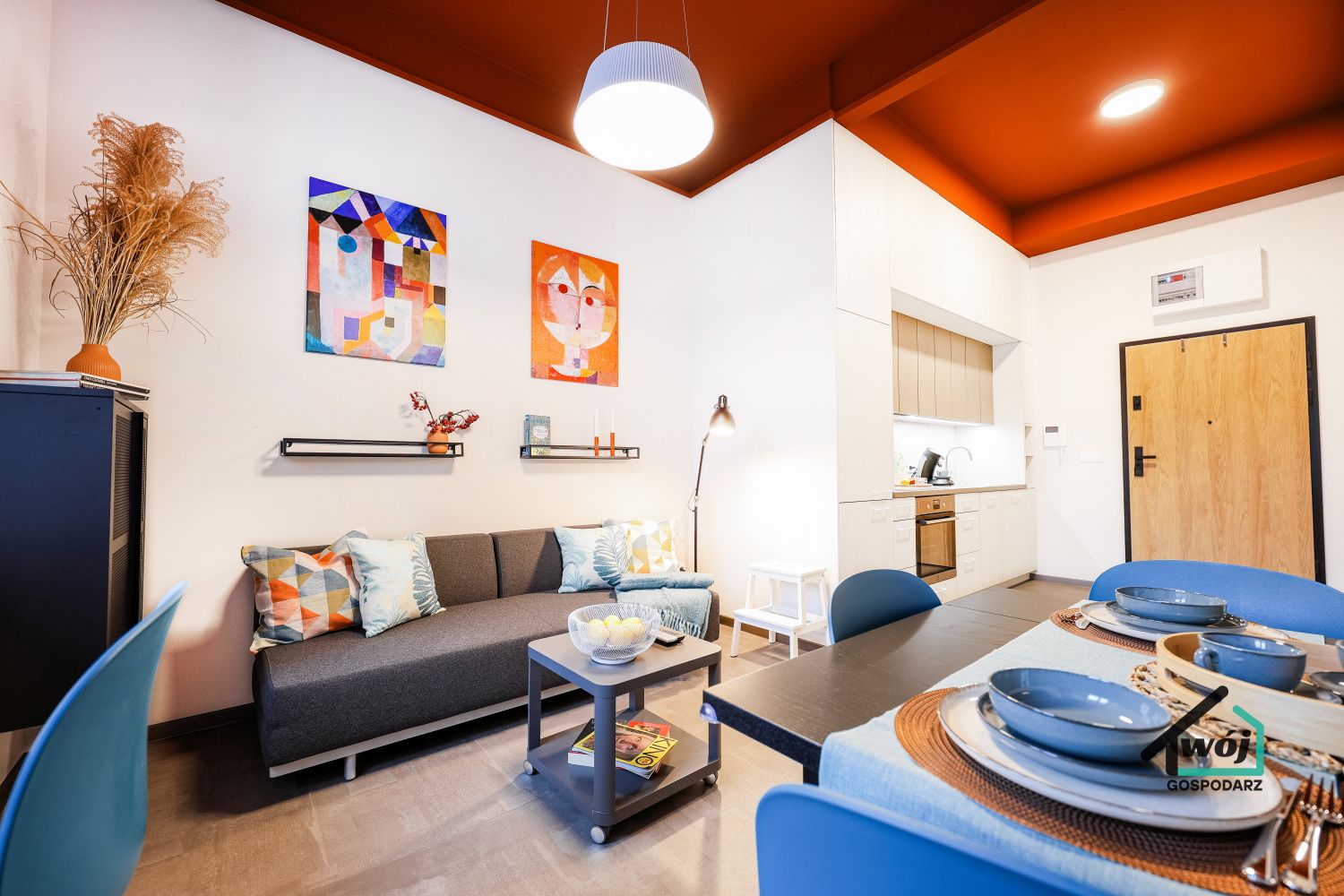 Salon apartamentu City Vibe Łódź z sofą, stołem jadalnianym i designerskim pomarańczowym sufitem